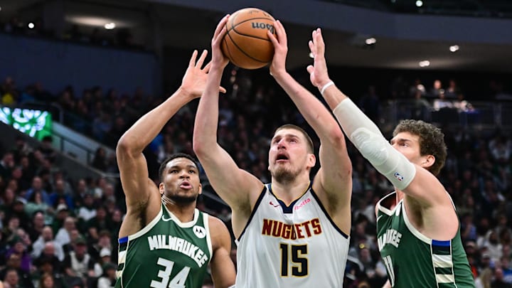 Feb 27, 2025; Milwaukee, Wisconsin, USA; Denver Nuggets center Nikola Jokic (15) takes a shot against Milwaukee Bucks forward Giannis Antetokounmpo (34) and center Brook Lopez (11) in the third quarter at Fiserv Forum. Mandatory Credit: Benny Sieu-Imagn Images