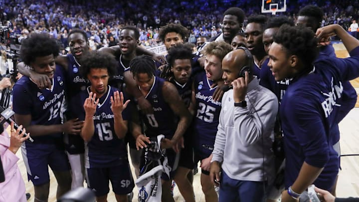 Saint Peter's players celebrate around head coach Shaheen Holloway as he does a television interview after the Peacocks' 67-64 win against Purdue to advance to the Elite Eight in the NCAA tournament at the Wells Fargo Center in Philadelphia, March 25, 2022.