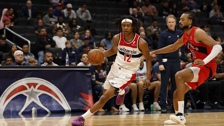 Oct 12, 2025; Washington, District of Columbia, USA; Washington Wizards guard Tre Johnson (12) drives to the basket as Toronto Raptors center Olivier Sarr (11) defends in the second half at Capital One Arena. Mandatory Credit: Geoff Burke-Imagn Images