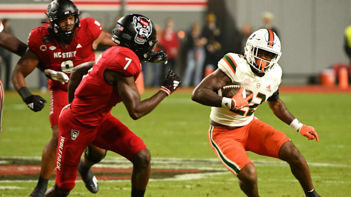Nov 4, 2023; Raleigh, North Carolina, USA; Miami Hurricanes running back Mark Fletcher Jr. (22) runs as North Carolina State Wolfpack cornerback Shyheim Battle (7) defends during the first half at Carter-Finley Stadium. Mandatory Credit: Rob Kinnan-Imagn Images