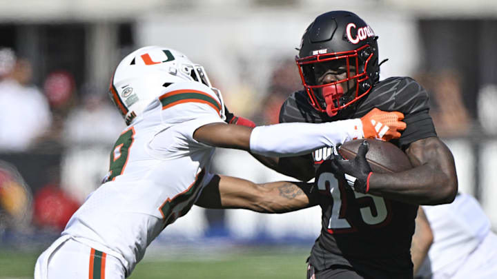 Oct 19, 2024; Louisville, Kentucky, USA; Louisville Cardinals running back Isaac Brown (25) runs the ball against Miami Hurricanes defensive back D'Yoni Hill (19) during the first half at L&N Federal Credit Union Stadium. Mandatory Credit: Jamie Rhodes-Imagn Images