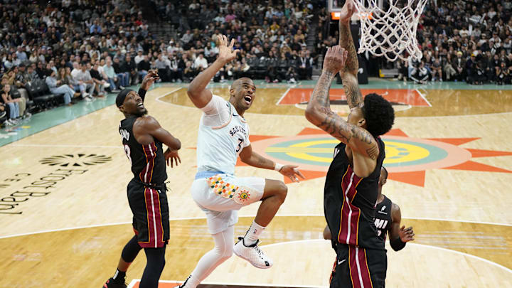 Feb 1, 2025; San Antonio, Texas, USA; San Antonio Spurs guard Chris Paul (3) reacts after shooting while defended by Miami Heat centers Kel'el Ware (7) and Bam Adebayo (13) during the second half at Frost Bank Center. Mandatory Credit: Scott Wachter-Imagn Images