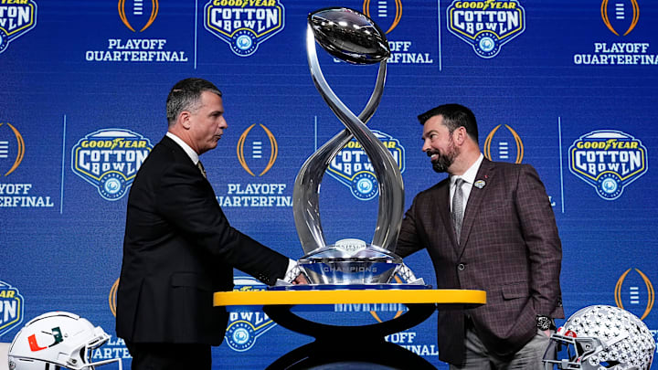 Ohio State Buckeyes head coach Ryan Day, right, and Miami (FL) Hurricanes head coach Mario Cristobal shake hands behind the Field Scovell Trophy after talking to media during a Cotton Bowl press conference at AT&T Stadium in Arlington, Texas prior to their College Football Playoff quarterfinal matchup on Dec. 30, 2025.