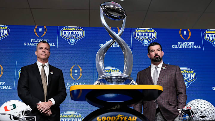 Ohio State Buckeyes head coach Ryan Day, right, and Miami (FL) Hurricanes head coach Mario Cristobal pose with the Field Scovell Trophy after talking to media during a Cotton Bowl press conference at AT&T Stadium in Arlington, Texas prior to their College Football Playoff quarterfinal matchup on Dec. 30, 2025.