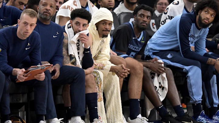 Mar 21, 2025; Inglewood, California, USA;  Memphis Grizzlies guard Ja Morant (12), center in white hoodie, looks on from the bench in the first half against the Los Angeles Clippers at Intuit Dome. Mandatory Credit: Jayne Kamin-Oncea-Imagn Images