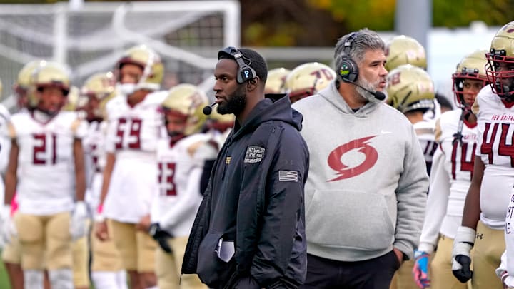 New Britain High School football coach Isaiah Boddie (center) stands on the sidelines during his team's game against the Maloney Spartans last season at Falcon Field in Meriden, Connecticut. 
