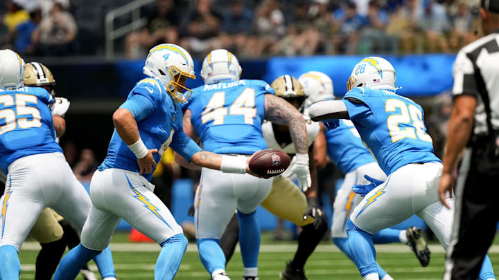 Aug 10, 2025; Inglewood, California, USA; Los Angeles Chargers quarterback Taylor Heinicke (4) hands off to running back Hassan Haskins (28) against the New Orleans Saints at SoFi Stadium. 