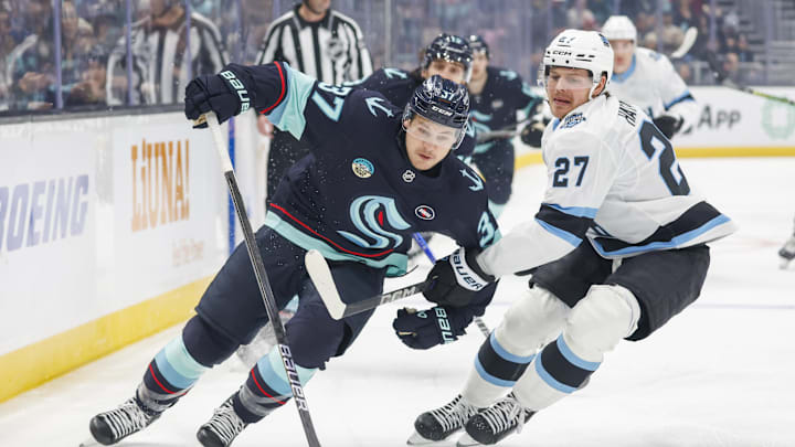 Dec 30, 2024; Seattle, Washington, USA; Seattle Kraken center Yanni Gourde (37) skates with the puck ahead of Utah Hockey Club center Barrett Hayton (27) during the first period at Climate Pledge Arena. Mandatory Credit: Joe Nicholson-Imagn Images