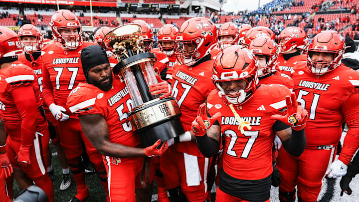 Louisville Cardinals defensive lineman Clev Lubin (50) holds the hefty Governors Cup trophy as Louisville Cardinals defensive back Jojo Evans Jr. (27) holds up the Ls after they dominated the Wildcats 41-0 Saturday, November 29, 2025 in Louisville, Kentucky at L&N Federal Credit Union Stadium.