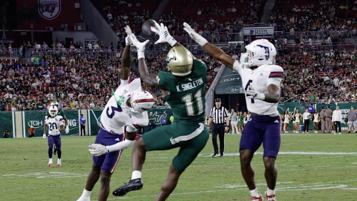 Oct 18, 2025; Tampa, Florida, USA;  South Florida Bulls wide receiver Keshaun Singleton (11) catches a pass between Florida Atlantic Owls defensive back Derrick Rogers Jr. (3) and defensive back Dillion Williams (4) during the second half at Raymond James Stadium. Mandatory Credit: Reinhold Matay-Imagn Images