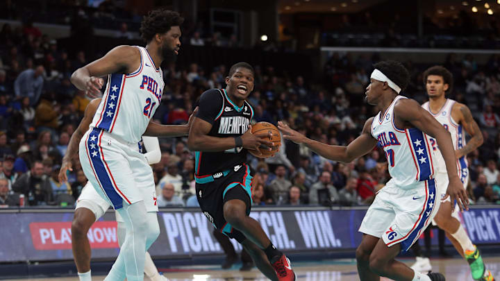 Dec 30, 2025; Memphis, Tennessee, USA; Memphis Grizzlies forward Cedric Coward (23) drives to the basket between Philadelphia 76ers center Joel Embiid (21) and guard VJ Edgecombe (77) during the third quarter at FedExForum. Mandatory Credit: Petre Thomas-Imagn Images