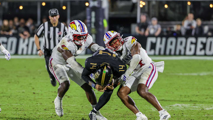Oct 4, 2025; Orlando, Florida, USA; UCF Knights quarterback Cam Fancher (14) is tackled by Kansas Jayhawks linebacker Trey Lathan (4) and safety Jalen Dye (14) during the second half at FBC Mortgage Stadium. Mandatory Credit: Mike Watters-Imagn Images