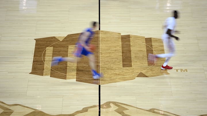 A blurred image of the center court logo as a Boise State Broncos player and a UNLV Rebels player run upcourt during the first half of a Mountain West Conference tournament game at Thomas Mack Center. 