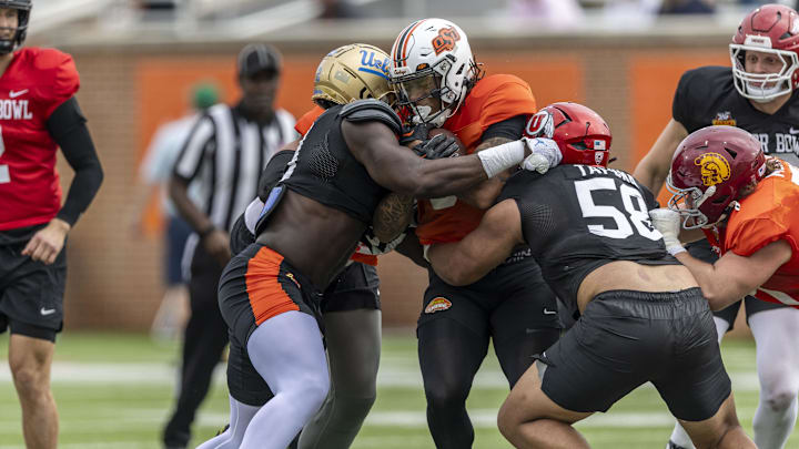 Jan 30, 2025; Mobile, AL, USA; National team defensive lineman Oluwafemi Oladejo of UCLA (99) and National team defensive lineman Junior Tafuna of Utah (58) tackle National team running back Ollie Gordon II of Oklahoma State (0) during Senior Bowl practice for the National team at Hancock Whitney Stadium. Mandatory Credit: Vasha Hunt-Imagn Images Jan 30, 2025; Mobile, AL, USA; National team defensive lineman Oluwafemi Oladejo of UCLA (99) and National team defensive lineman Junior Tafuna of Utah (58) tackle National team running back Ollie Gordon II of Oklahoma State (0) during Senior Bowl practice for the National team at Hancock Whitney Stadium. Mandatory Credit: Vasha Hunt-Imagn Images