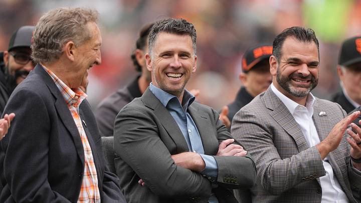 Apr 25, 2026; San Francisco, California, USA; San Francisco Giants president of baseball operations Buster Posey (center) sits on the field with president Larry Baer (left) and general manager Zack Minasian (right) before the game against the Miami Marlins at Oracle Park. Mandatory Credit: Darren Yamashita-Imagn Images