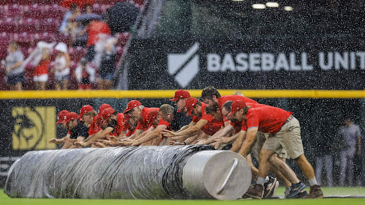 Jul 9, 2024; Cincinnati, Ohio, USA; Members of the grounds crew roll out the tarp during a rain delay in the third inning in the game between the Colorado Rockies and the Cincinnati Reds at Great American Ball Park. Mandatory Credit: Katie Stratman-Imagn Images