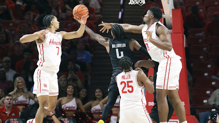 Nov 8, 2025; Houston, Texas, USA; Towson Tigers guard Dylan Williamson (4) shoots the ball as Houston Cougars guard Milos Uzan (7) and center Cedric Lath (8) defend during the first half at Fertitta Center. Mandatory Credit: Troy Taormina-Imagn Images