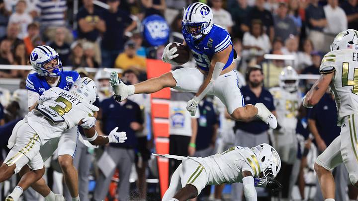 Dec 27, 2025; Orlando, FL, USA; BYU Cougars running back Enoch Nawahine (21) jumps over Georgia Tech Yellow Jackets defensive back Omar Daniels (9) during the second half at Camping World Stadium. Mandatory Credit: Kim Klement Neitzel-Imagn Images