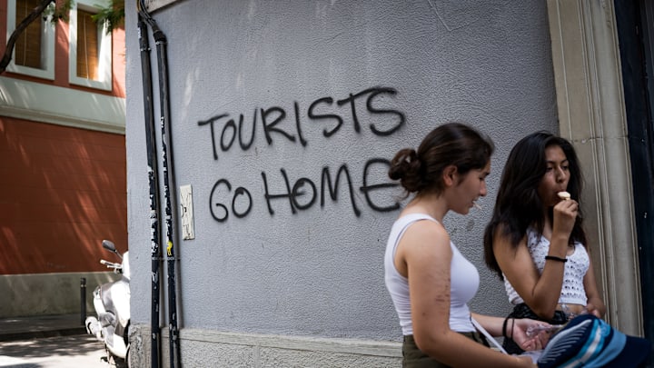 People seen next to a graffiti reading "tourists go home" on...
