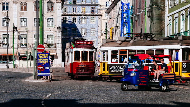 Tuk-tuk carrying tourists, classic trams and buildings in "...