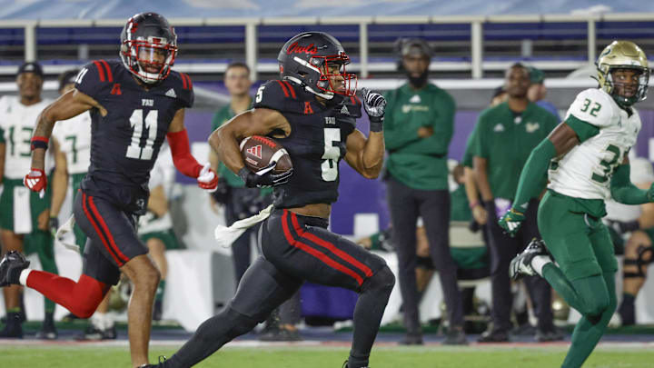 Nov 1, 2024; Boca Raton, Florida, USA;  Florida Atlantic Owls running back CJ Campbell Jr. (5) runs the ball getting past South Florida Bulls defensive back James Chenault (32) as Owls wide receiver Marlyn Johnson (11) follows along during the second half at FAU Stadium. Mandatory Credit: Reinhold Matay-Imagn Images