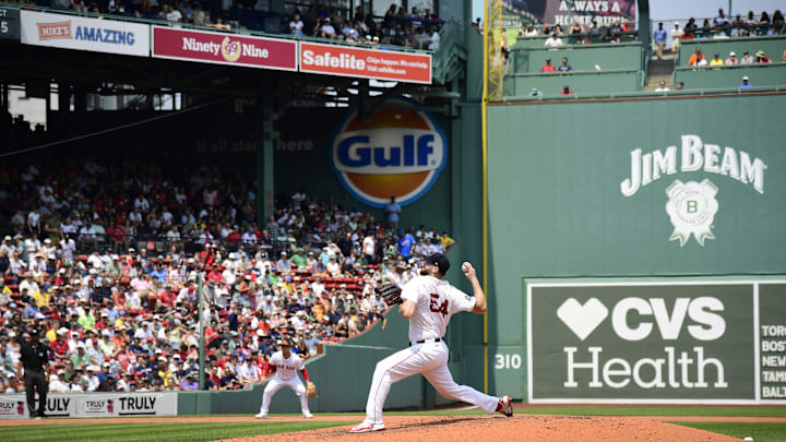 Boston Red Sox pitcher Lucas Giolito throws a pitch, wearing a white jersey and dark blue hat, Fenway Park in the background.