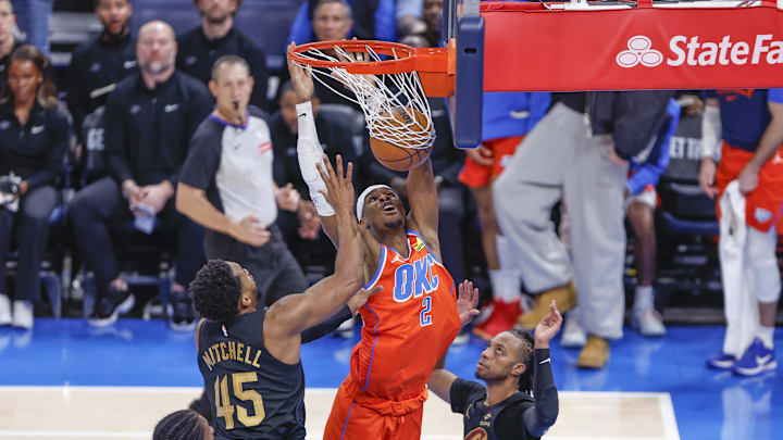 Jan 16, 2025; Oklahoma City, Oklahoma, USA; Oklahoma City Thunder guard Shai Gilgeous-Alexander (2) dunks between Cleveland Cavaliers guard Darius Garland (10) and guard Donovan Mitchell (45) during the fourth quarter at Paycom Center. Mandatory Credit: Alonzo Adams-Imagn Images