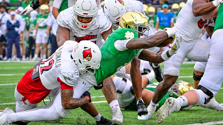 Sep 28, 2024; South Bend, Indiana, USA; Notre Dame Fighting Irish running back Jeremiyah Love (4) stretches the ball across the goal line for a touchdown against Louisville Cardinals safety Tamarion McDonald (12) in the first quarter at Notre Dame Stadium. Mandatory Credit: Matt Cashore-Imagn Images