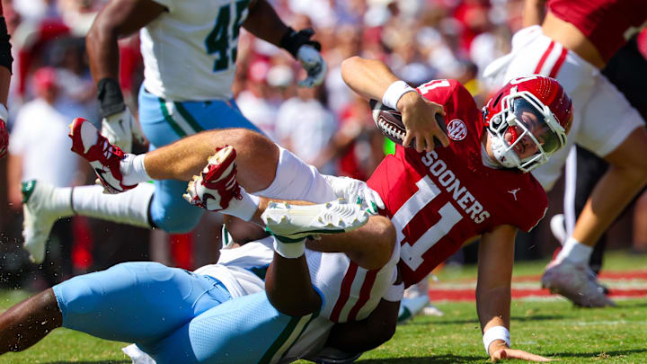 Tulane defender Sam Arnold tackles a ball carrier while wearing a white jersey and teal pants. 