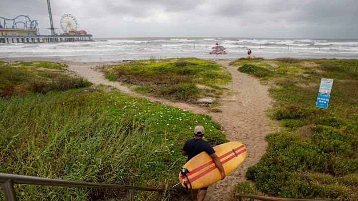 A surfer walks down to the beach on Wednesday, Aug. 25, 2020, near Galveston Island Historic Pleasure Pier.