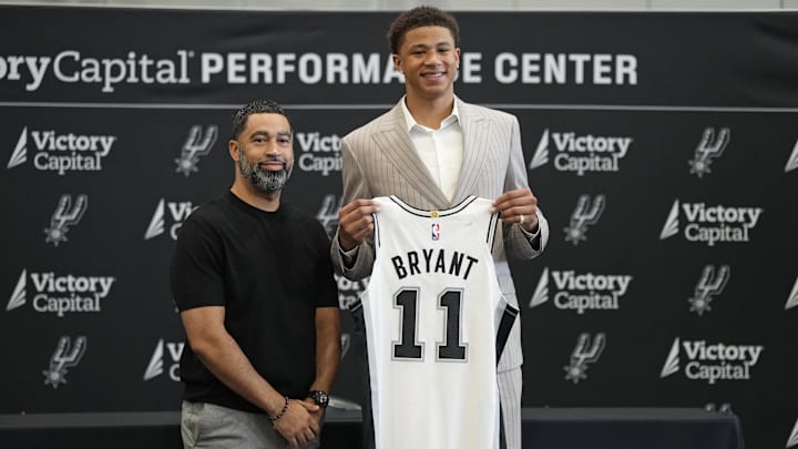 Jun 28, 2025; San Antonio, TX, USA; San Antonio first round draft pick Carter Bryant (11) holds up his jersey along with general manager Brian Wright at Victory Capital Performance Center. Mandatory Credit: Scott Wachter-Imagn Images