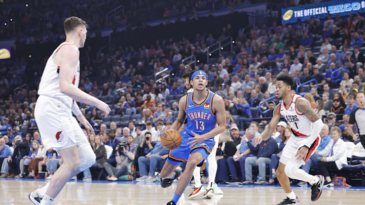 Mar 7, 2025; Oklahoma City, Oklahoma, USA; Oklahoma City Thunder forward Ousmane Dieng (13) drives to the basket between Portland Trail Blazers center Donovan Clingan (23) and guard Anfernee Simons (1) during the first quarter at Paycom Center. Mandatory Credit: Alonzo Adams-Imagn Images