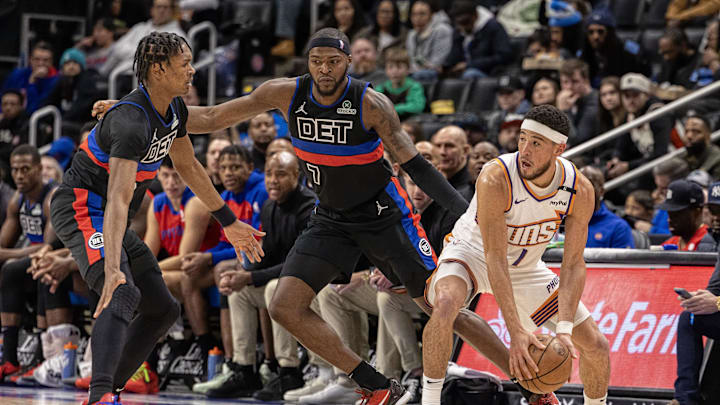 Jan 18, 2025; Detroit, Michigan, USA; Phoenix Suns guard Devin Booker (1) controls the ball in front of Detroit Pistons forward Paul Reed (7) and forward Ausar Thompson (9) during the second quarter at Little Caesars Arena. Mandatory Credit: David Reginek-Imagn Images