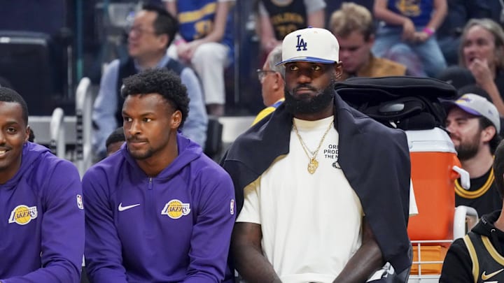 Oct 5, 2025; San Francisco, California, USA;   Los Angeles Lakers guard Bronny James (9) and forward LeBron James (23), wearing a Los Angeles Dodgers cap, watch the action against the Golden State Warriors in the first quarter at Chase Center. Mandatory Credit: David Gonzales-Imagn Images