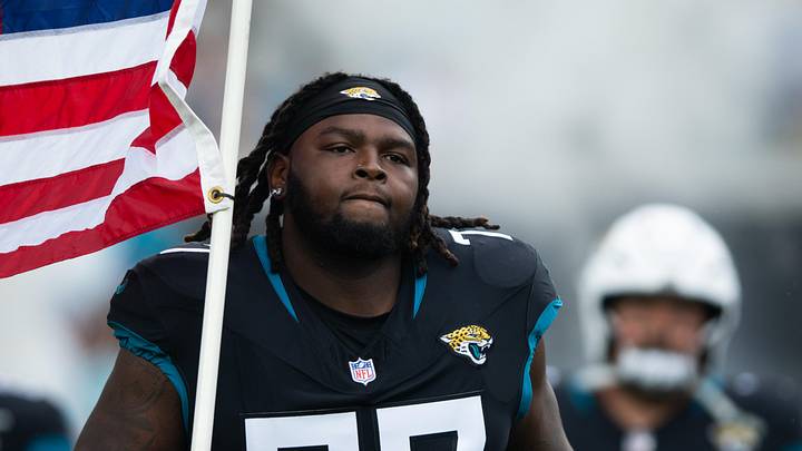 Nov 10, 2024; Jacksonville, Florida, USA;  Jacksonville Jaguars offensive lineman Anton Harrison (77) runs onto the field with the American flag before the. game against the Minnesota Vikings at EverBank Stadium. Mandatory Credit: Jeremy Reper-Imagn Images