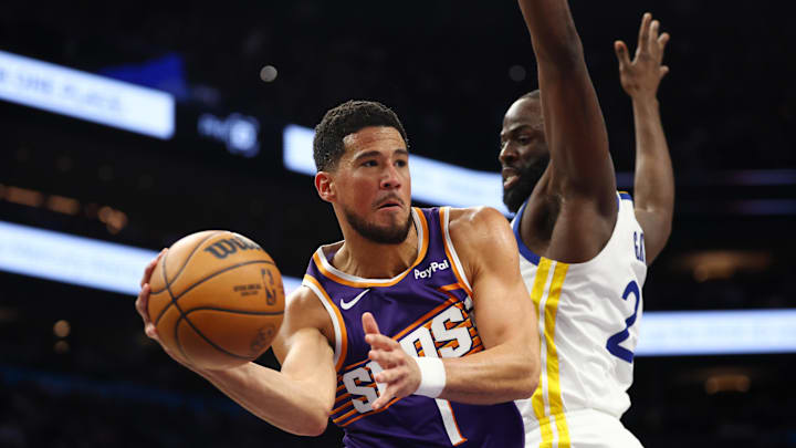 Dec 18, 2025; Phoenix, Arizona, USA; Phoenix Suns guard Devin Booker (1) passes the ball against Golden State Warriors forward Draymond Green (23) in the second half at Mortgage Matchup Center. Mandatory Credit: Mark J. Rebilas-Imagn Images