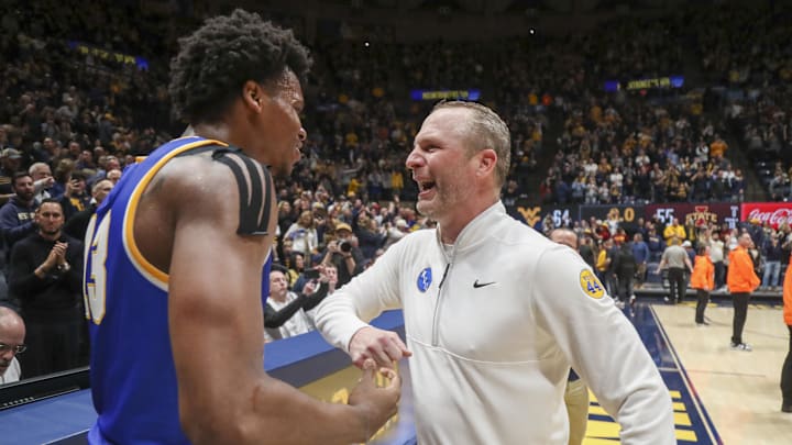 Jan 18, 2025; Morgantown, West Virginia, USA; West Virginia Mountaineers head coach Darian DeVries celebrates with West Virginia Mountaineers forward Amani Hansberry (13) after defeating the Iowa State Cyclones at WVU Coliseum. Mandatory Credit: Ben Queen-Imagn Images