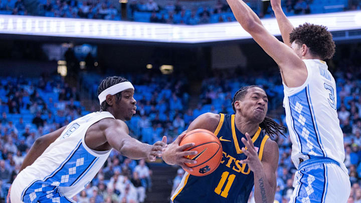 Dec 16, 2025; Chapel Hill, North Carolina, USA; ETSU Buccaneers guard Brian Taylor (11) drives between North Carolina Tar Heels forward Caleb Wilson (8) and guard Derek Dixon (3) during the first half at Dean E. Smith Center. Mandatory Credit: Scott Kinser-Imagn Images