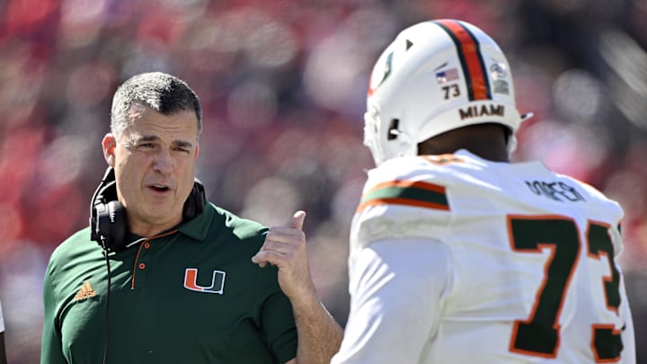 Oct 19, 2024; Louisville, Kentucky, USA; Miami Hurricanes head coach Mario Cristobal talks with offensive lineman Anez Cooper (73) during the first half against the Louisville Cardinals at L&N Federal Credit Union Stadium. Mandatory Credit: Jamie Rhodes-Imagn Images