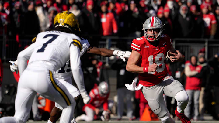 Ohio State Buckeyes quarterback Will Howard (18) is pursued by Michigan Wolverines defensive back Makari Paige (7) and Michigan Wolverines linebacker Ernest Hausmann (15 )during the first half of Saturday’s NCAA Division I football game at Ohio Stadium.