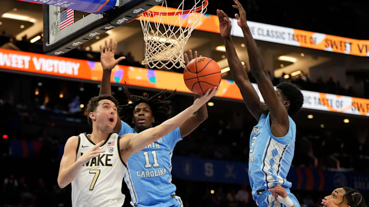 Mar 13, 2025; Charlotte, NC, USA; Wake Forest Demon Deacons guard Parker Friedrichsen (7) shoots as North Carolina Tar Heels guard Ian Jackson (11) and guard Drake Powell (9) defend in the first half at Spectrum Center. Mandatory Credit: Bob Donnan-Imagn Images