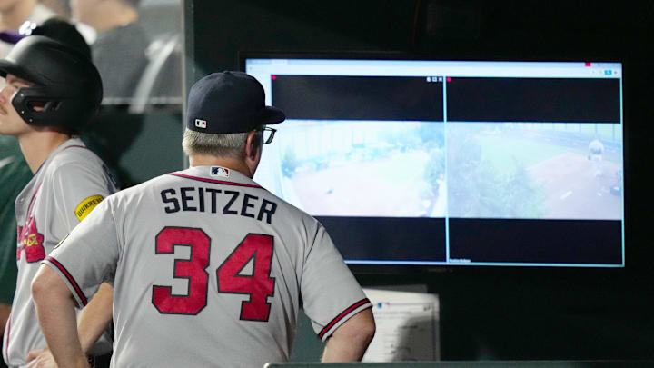 Atlanta Braves hitting coach Kevin Seitzer (34) looks at the bull pen monitors in the seventh inning against the Colorado Rockies at Coors Field. 