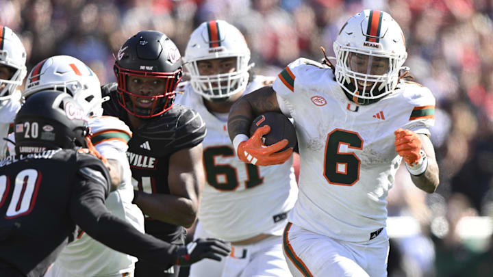 Oct 19, 2024; Louisville, Kentucky, USA; Miami Hurricanes running back Damien Martinez (6) runs the ball against Louisville Cardinals defensive back Tayon Holloway (20)  during the second half at L&N Federal Credit Union Stadium. Miami defeated Louisville 52-45. Mandatory Credit: Jamie Rhodes-Imagn Images