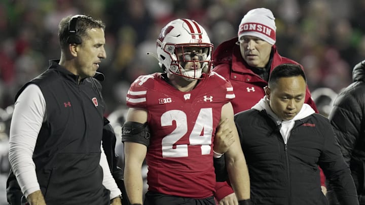 Nov 16, 2024; Madison, Wisconsin, USA; Wisconsin Badgers head coach Luke Fickell (left) helps safety Hunter Wohler (24) get off the field after suffering an apparent injury during the fourth quarter against the Oregon Ducks at Camp Randall Stadium. Oregon won 16-13. Mandatory Credit: Mark Hoffman/USA TODAY Network via Imagn Images