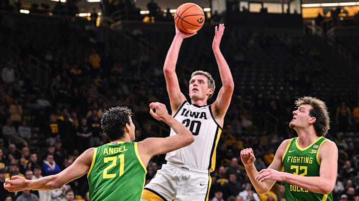 Feb 19, 2025; Iowa City, Iowa, USA; Iowa Hawkeyes forward Payton Sandfort (20) goes to the basket as Oregon Ducks forward Brandon Angel (21) and center Nate Bittle (32) defend during the second half at Carver-Hawkeye Arena. Mandatory Credit: Jeffrey Becker-Imagn Images