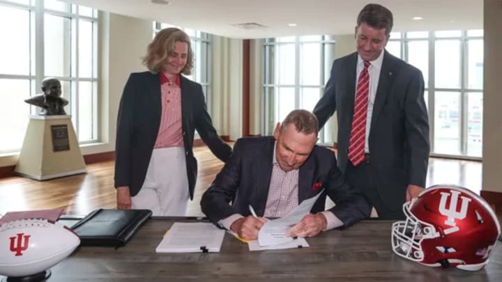 Merchants Bank chairman Mike Petrie signs a contract surrounded by Indiana President Pamela Whitten (left) and athletic director Scott Dolson (right).