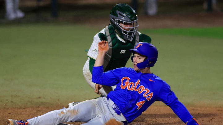 Florida infielder Cade Kurland (4) scores against Jacksonville catcher Nick DeLisi (38) during the eighth inning of an NCAA baseball matchup.