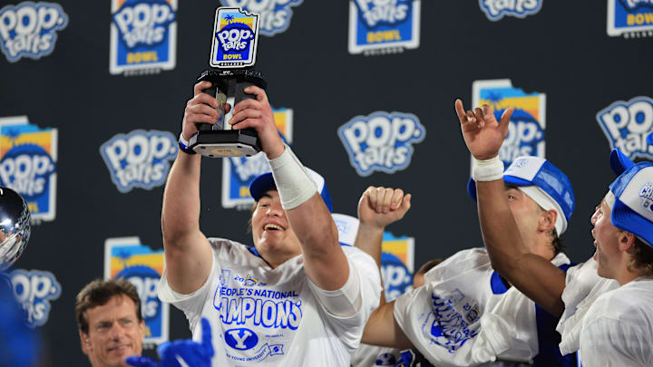 Dec 27, 2025; Orlando, FL, USA; BYU Cougars quarterback Bear Bachmeier (47) is presented the MVP trophy and celebrates after they beat the against the Georgia Tech Yellow Jackets at Camping World Stadium. Mandatory Credit: Kim Klement Neitzel-Imagn Images
