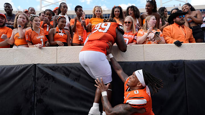 Oklahoma State's Ollie Gordon II (0) helps Iman Oates (99) off the wall following the college football game between the Oklahoma State Cowboys and South Dakota State Jackrabbits at Boone Pickens Stadium in Stillwater, Okla., Saturday, Aug., 31, 2024.