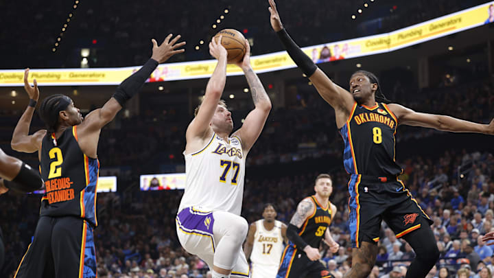 Apr 6, 2025; Oklahoma City, Oklahoma, USA; Los Angeles Lakers guard Luka Doncic (77) drives to the basket between Oklahoma City Thunder guard Shai Gilgeous-Alexander (2) and forward Jalen Williams (8) during the second quarter at Paycom Center. Mandatory Credit: Alonzo Adams-Imagn Images